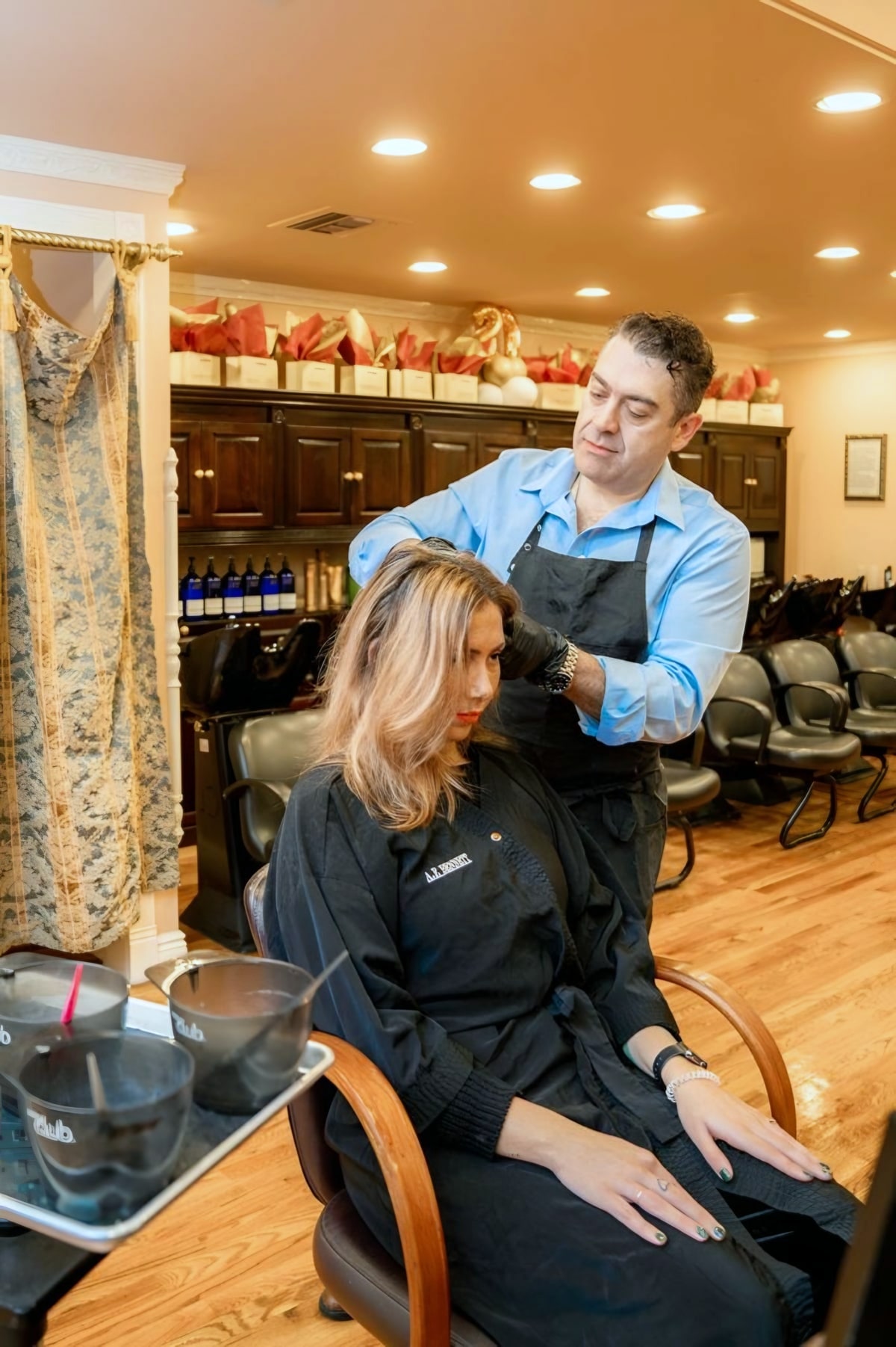 Male stylist applying hair color to seated client in salon