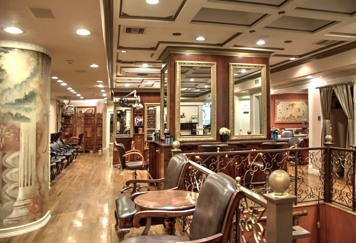 Salon interior with gilt mirrors, wood floor, leather chairs, and iron railing
